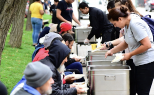 homeless people being served food in a park during the day time
