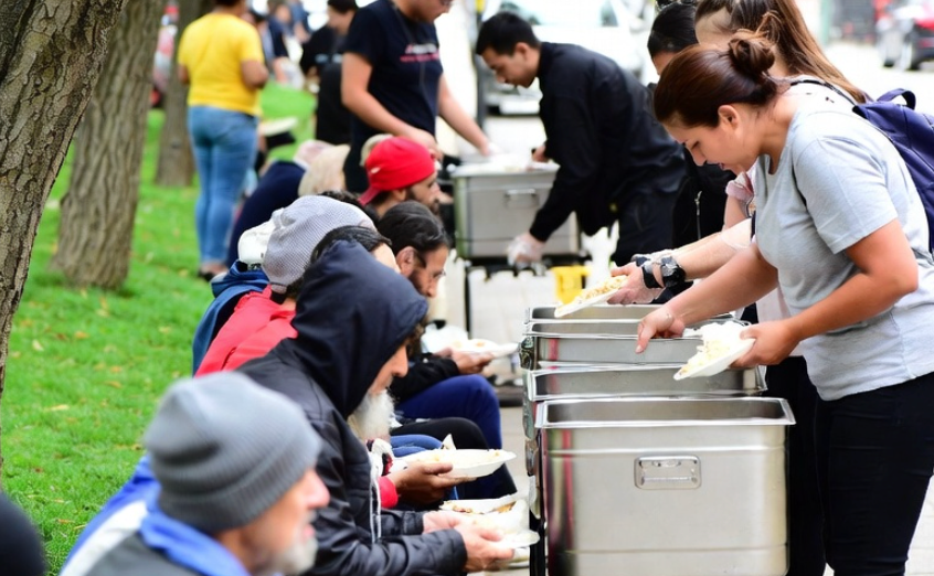 homeless people being served food in a park during the day time