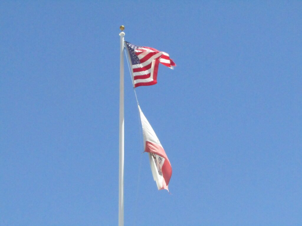 California and USA flags flying on a pole with blue sky background during day