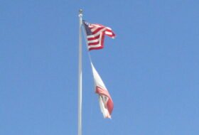California and USA flags flying on a pole with blue sky background during day