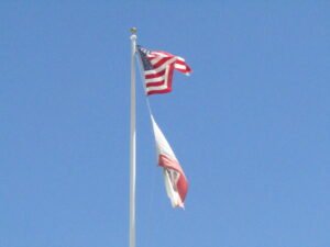 California and USA flags flying on a pole with blue sky background during day