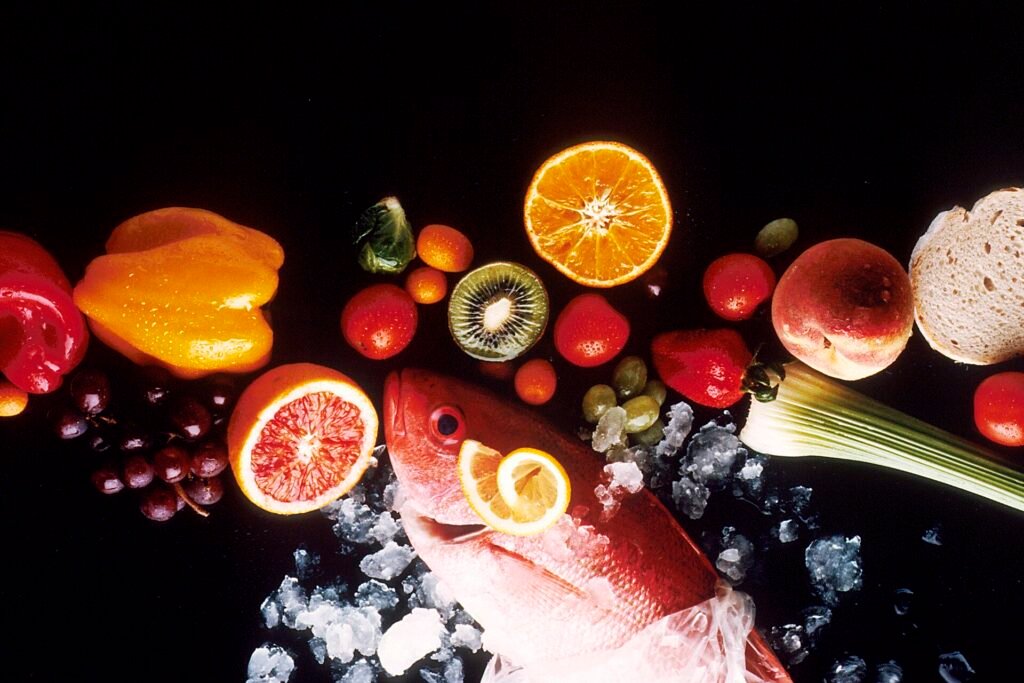 fruits, vegetables, and a fish laid out on top of a table
