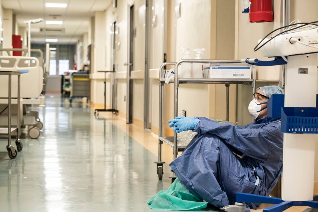 masked healthcare worker sitting on the ground inside hospital