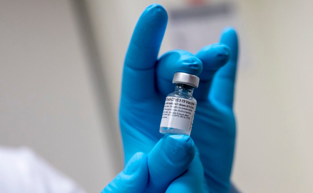 Person with gloves holding COVID vaccine vial