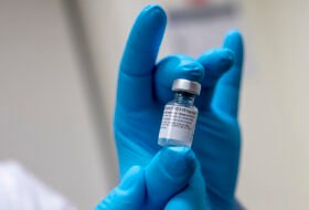 Person with gloves holding COVID vaccine vial